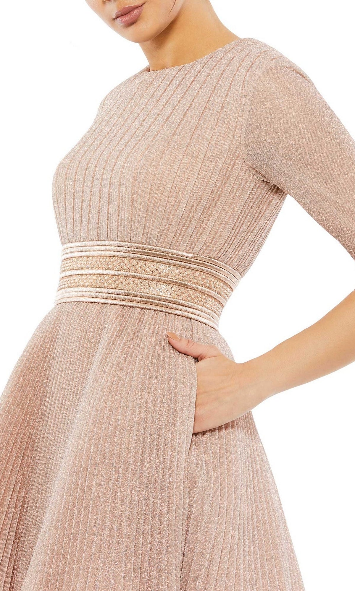 A woman models the Short Party Dress 30749 by Mac Duggal—a light pink pleated A-line party dress with long sleeves, metallic banded waist, and pockets—shown from shoulders to hips, with one hand in a pocket.